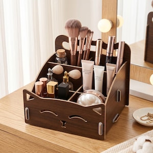 May include: A dark brown wooden makeup organizer with a cat-shaped silhouette featuring cutouts for eyes and a nose. The organizer has multiple compartments filled with various cosmetic items, including makeup brushes, tubes, and small glass bottles.
