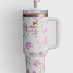 Op de afbeelding: Witte ge&iuml;soleerde beker met een rozenpatroon en een roze strik op het rietje. De beker heeft een handvat en de tekst "STANLEY" en "LOVESHAKE".