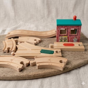 Könnte beinhalten: Holzspielzeug-Eisenbahn-Set mit einem rot-grünen Stall, verschiedenen Gleisstücken und einer Holzbasis. Der Stall trägt den Text "PIG FEED". Die Gleisstücke umfassen gebogene und gerade Abschnitte sowie eine Weiche. Für Kinder.