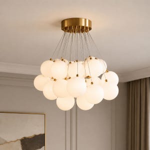 May include: A contemporary chandelier with numerous spherical, frosted glass globes hanging from a brass-coloured ceiling mount. The globes are arranged in a cluster, providing a soft, ambient light source for interior spaces.