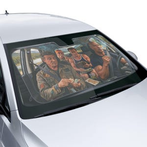 May include: A car windshield sunshade featuring a printed graphic of four individuals sitting inside a vehicle. The image depicts a realistic scene with figures resembling action movie stars, including one person in a tan jacket and another in a black shirt.