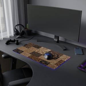 May include: A rectangular mouse pad featuring a patchwork design of brown, tan, and black floral damask patterns. The mouse pad has a thin, glowing blue LED light strip along its edge and is positioned on a dark desk with a computer mouse on top.
