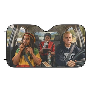May include: A car sunshade featuring a graphic print of Bob Marley, Michael Jackson, and Eminem sitting inside a vehicle. Bob Marley wears a rasta-colored hat and shirt, Michael Jackson wears a red jacket, and Eminem wears a dark blue hoodie.