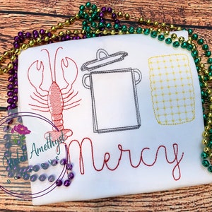 May include: A white t-shirt with red embroidery of a lobster, a pot with a lid, and a jar of corn. The name "Mercy" is embroidered in red below the images.