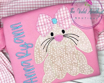 May include: Pink children's shirt with a light brown bunny applique with a pink nose and blue bow. The shirt has the text "Happy Easter" embroidered in blue.