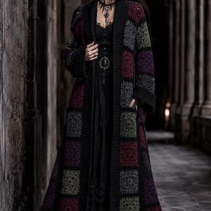 May include: A long, open-front cardigan featuring a patchwork design of crocheted granny squares in shades of black, deep red, olive green, and grey. The garment has long sleeves, a solid black ribbed trim along the front opening, and side pockets.