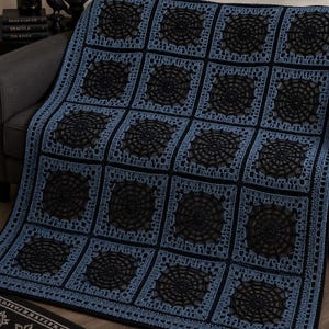 Puede incluir: Una manta de ganchillo rectangular con un patrón de cuadrícula repetitivo de motivos cuadrados. Cada cuadrado contiene un diseño de telaraña circular negra dentro de un borde azul polvoriento. La manta tiene un borde de ganchillo negro.