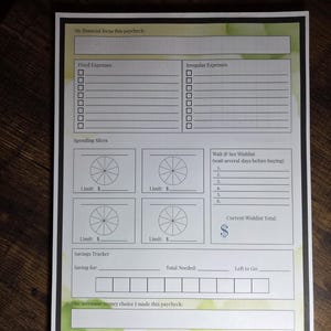Könnte beinhalten: Ein weißes und grünes Finanzplanungsblatt mit Abschnitten für feste und unregelmäßige Ausgaben, Ausgabenscheiben und einen Spar-Tracker. Der Text "My financial focus this paycheck" steht oben.