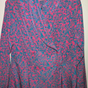 Könnte beinhalten: Ein doppelreihiger Blazer in leuchtendem Pink, verziert mit einem türkisblauen Wirbelmuster. Die langärmlige Jacke hat einen Reverskragen und Knöpfe und bietet ein auffälliges, gemustertes Kleidungsstück.