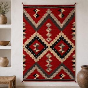 May include: A rectangular wall hanging rug featuring a bold red background with a repeating geometric pattern in black, cream, and gray. The design includes large diamonds and zigzag chevrons, finished with small tassels at the top and bottom corners.