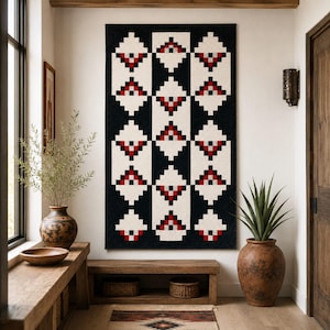May include: A rectangular wall hanging featuring a geometric pixelated pattern in black, white, and red. The design consists of repeating diamond shapes arranged in vertical columns, creating a structured, symmetrical, and high-contrast visual display.