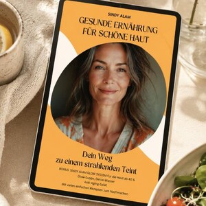 Può includere: Un tablet mostra la copertina di un libro con il titolo "GESUNDE ERNÄHRUNG FÜR SCHÖNE HAUT" e un ritratto di donna. La copertina è arancione con testo bianco. Il tablet è su una superficie beige, con una tazza e insalata sullo sfondo.