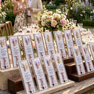 Pu&ograve; includere: Un'impostazione della tavola con diverse penne regalo in confezioni trasparenti, ognuna con un design floreale e il testo "Thank you for celebrating with us". La scena comprende un centrotavola floreale, una coppia e un'ambientazione in giardino.