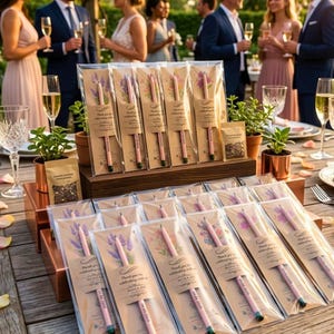 May include: Wedding favors featuring pink pencils with floral designs and the text "Thank you for celebrating with us." The pencils are packaged in clear plastic with a kraft paper backing. The scene includes guests at an outdoor event with champagne.