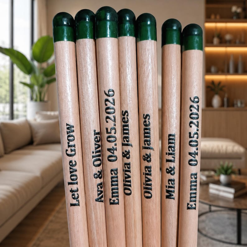 Puede incluir: Siete palos cil&iacute;ndricos de madera con puntas pintadas de verde oscuro. Cada palo presenta texto grabado en negro que incluye nombres como Ava & Oliver, Mia & Liam y Olivia & James, la fecha 04.05.2026 y la frase Let love Grow.