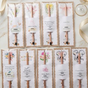 May include: Ten wooden pencils, each individually packaged in a clear sleeve with a decorative card backing. The cards feature various floral, birthday, and castle illustrations with custom text including names like Emma and Liam and dates.