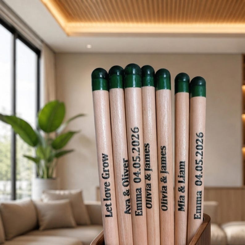 Puede incluir: Una colecci&oacute;n de siete l&aacute;pices de madera clara con puntas pintadas en verde oscuro. Cada l&aacute;piz est&aacute; grabado con texto negro, incluyendo nombres como Ava & Oliver, Olivia & James y Mia & Liam, la fecha 04.05.2026 y la frase Let love Grow.