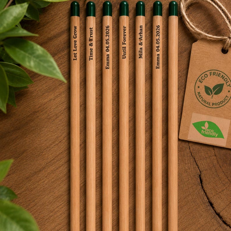 Puede incluir: Siete l&aacute;pices de madera clara con gomas de borrar verde oscuro, cada uno con texto impreso en negro que incluye Let Love Grow, Time & Trust, Emma 04.05.2026, Until Forever, Mila & Arhan y Emma 04.05.2026, junto a una etiqueta de papel.