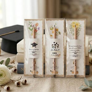 May include: Three personalized wooden pencils, each encased in a clear plastic sleeve with a decorative card backing. The cards feature floral illustrations and graduation-themed text, including names like Emma and Suna, and dates for graduation.