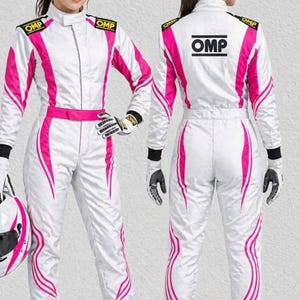 May include: A white racing suit with vibrant pink side panels and stripes, featuring the black OMP logo on the shoulders and back. The suit includes a high collar, a waist belt, and matching gloves, with a white and pink helmet held at the side.