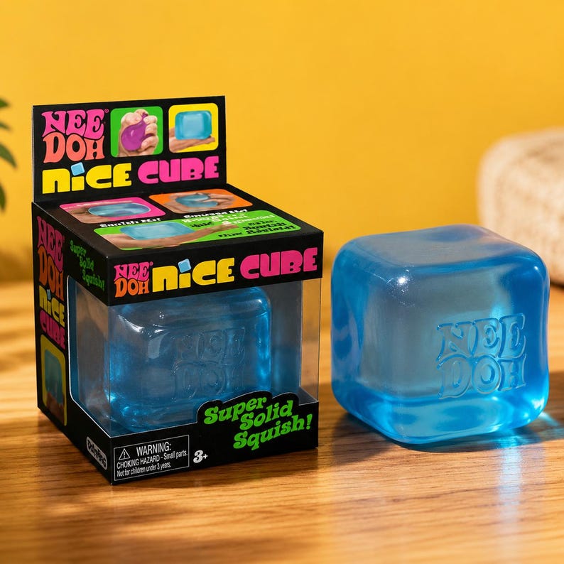 May include: A translucent blue squishy cube toy labeled Nee Doh Nice Cube in its black cardboard retail box. The box features bright pink and yellow text, product images, and the phrase Super Solid Squish. The cube itself is a solid blue square.