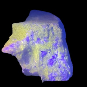Puede incluir: Primer plano de un espécimen mineral con una forma rugosa e irregular. La roca presenta colores amarillo pálido y azul, con zonas de intenso púrpura. El fondo es negro, resaltando la coloración y textura únicas del mineral.