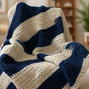 Op de afbeelding: Een handgemaakte, dik gebreide deken in marineblauwe en crèmekleurige strepen. De deken is over een stoel gedrapeerd, waarbij de textuur en het patroon worden getoond. Deze gezellige plaid is perfect om warmte en stijl toe te voegen aan elke woonruimte.
