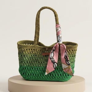 May include: A crochet tote bag featuring an ombre color gradient transitioning from olive green at the top to a vibrant grass green at the base. The bag includes two matching crochet handles and a decorative pink silk scarf tied to one handle.