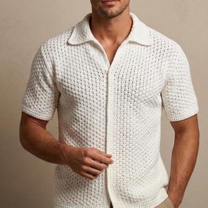May include: A short-sleeved, off-white knit shirt featuring a textured, open-weave pattern, a classic collar, and a full-length front button placket. The garment is constructed with a breathable, lightweight fabric and finished with ribbed cuffs.