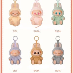 Puede incluir: Seis figuras de conejos de peluche en colores pastel, cada una con una expresi&oacute;n facial &uacute;nica y un llavero. Las figuras est&aacute;n etiquetadas con los nombres: SISI, DADA, QUQU, ZIZI, BABA y HEHE. Los conejos visten trajes con capucha.