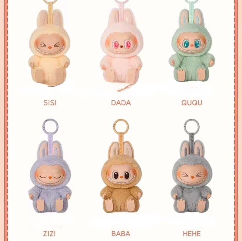 Puede incluir: Seis figuras de conejos de peluche en colores pastel, cada una con una expresi&oacute;n facial &uacute;nica y un llavero. Las figuras est&aacute;n etiquetadas con los nombres: SISI, DADA, QUQU, ZIZI, BABA y HEHE. Los conejos visten trajes con capucha.