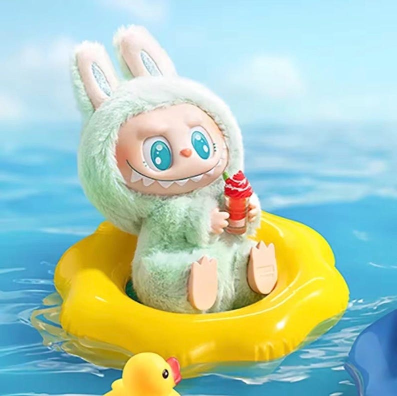 Puede incluir: Una figura caprichosa de un personaje parecido a un conejo con un atuendo verde difuso, sosteniendo un helado rojo. La figura est&aacute; sentada en un flotador inflable amarillo en el agua. Un patito de goma amarillo est&aacute; en primer plano.