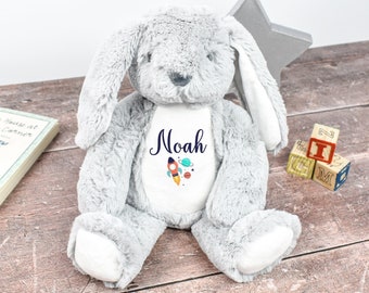May include: A gray plush bunny with long floppy ears. The bunny has a white patch on its chest with the name "Noah" embroidered in blue, along with a rocket ship and planets.