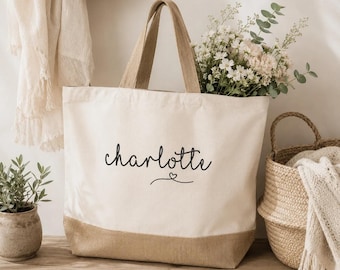 May include: A cream-colored canvas tote bag with a tan burlap base. The front of the bag features the name Charlotte printed in black script lettering, accompanied by a small heart icon centered below the name.