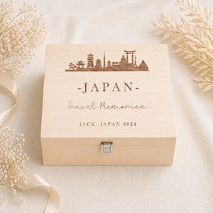 May include: A light-coloured wooden box with a hinged lid and a silver clasp. The lid features a laser-etched skyline of Japan, the word "-JAPAN-", and the text "Travel Memories". The box is personalised with "JACK- JAPAN 2024".