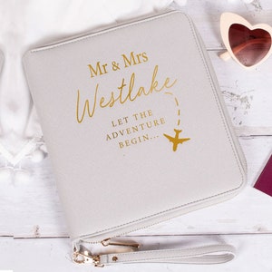 May include: A gray passport holder with a gold zipper and a gold inscription that reads "Mr. & Mrs. Westlake Let the Adventure Begin..." with a gold airplane icon.