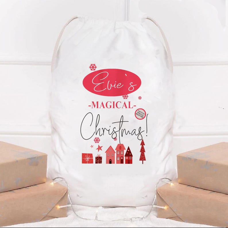 May include: A white Christmas gift sack with a drawstring closure. The sack features the text "Evie's -MAGICAL- Christmas!" in red and black, along with red illustrations of gifts, houses, and a Christmas tree. Presents wrapped in brown paper are in the foreground.