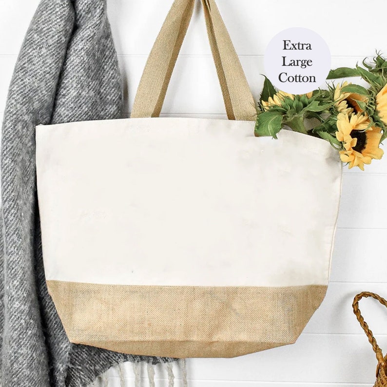 May include: A large, white canvas tote bag with a brown burlap bottom. The bag has two long brown straps and is hanging from a hook. The bag is labeled "Extra Large Cotton".