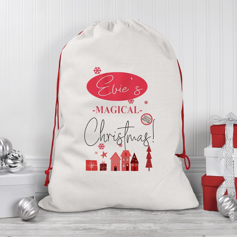 May include: A white Christmas gift sack with red drawstring closure. The sack features the text "Evie's -MAGICAL- Christmas!" in red and black, along with festive illustrations of houses, gifts, and a Christmas tree.
