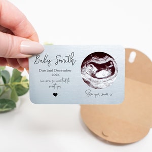 May include: A silver metal card with a black and white ultrasound image of a baby. The card says "Baby Smith Due 2nd December 2024 we are so excited to meet you See you soon x".