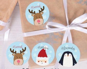 Könnte beinhalten: Runde Geschenkanhänger mit Rentier-, Weihnachtsmann- und Pinguin-Designs auf hellblauem Hintergrund. Die Anhänger tragen Namen wie "Hannah", "Harrison" und "Alexander". Der Text "3 Designs Available" ist sichtbar.