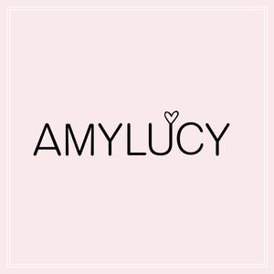 以下が含まれることがあります： 「AMYLUCY」というテキストと「Y」の上に小さなハートが描かれた白黒のロゴです。