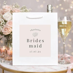 May include: A white ceramic mug with a black handle and the text "But First, Coffee" in a black, handwritten-style font. The mug is on a white surface.