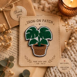 May include: An embroidered iron-on patch featuring a green monstera plant in a brown pot, centered on a rectangular tan card with the text IRON-ON PATCH, MADE WITH CARE - FOR YOU, and a small circular sticker labeled EASY TO APPLY LONG LASTING QUALITY.