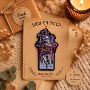 Puede incluir: Un parche bordado termoadhesivo que muestra un paisaje con una montaña, flores de cerezo, una puerta torii y una persona con un sombrero cónico. El parche está montado en una tarjeta rectangular con la etiqueta IRON-ON PATCH, MADE WITH CARE - FOR YOU.
