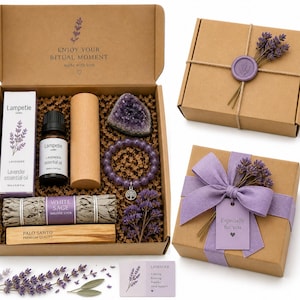 Può includere: Un set regalo a tema lavanda in una scatola di cartone. Include olio essenziale, un braccialetto, una geode, salvia, palo santo e un oggetto di legno. La scatola è decorata con un rametto di lavanda e il testo "Enjoy Your Ritual Moment".