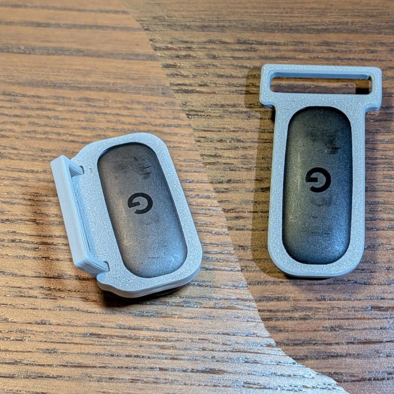 May include: Two rectangular clips featuring a light grey plastic frame and a dark grey centre insert. Each insert displays a lowercase letter G in the centre. One clip is positioned horizontally, while the other is oriented vertically.