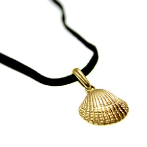 Puede incluir: Un collar con un colgante de concha dorada en un cordón de terciopelo negro.