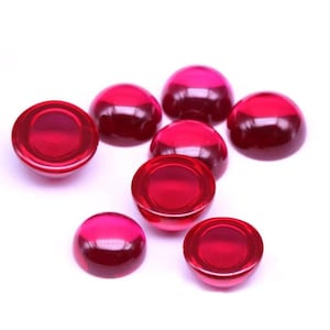 May include: A collection of eight smooth, translucent, circular cabochons in a vibrant ruby red color. Each piece features a domed top and a flat base, with a polished, glossy finish that reflects light, creating bright highlights across the surfaces.