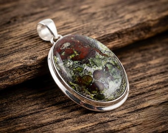 May include: An oval pendant featuring a polished, multi-colored stone with deep red, forest green, and black mottled patterns. The stone is set in a smooth, polished silver-toned metal bezel with a matching silver-toned bail at the top.